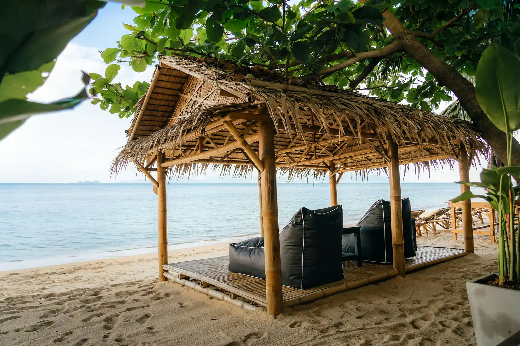 A bamboo sala with a thatched roof standing on the sand, looking out across calm sea.